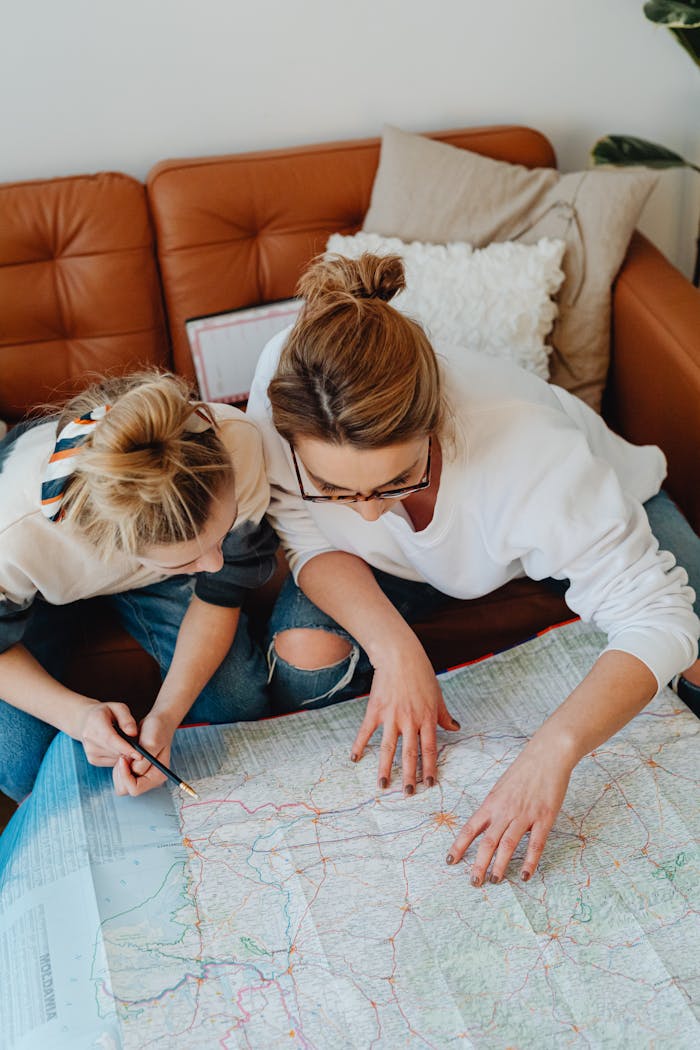 A mother and daughter planning a trip using a map while sitting on a sofa.